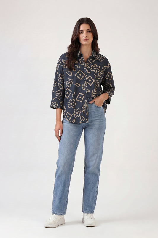 Woman wearing a patterned shirt and light blue jeans on a white background