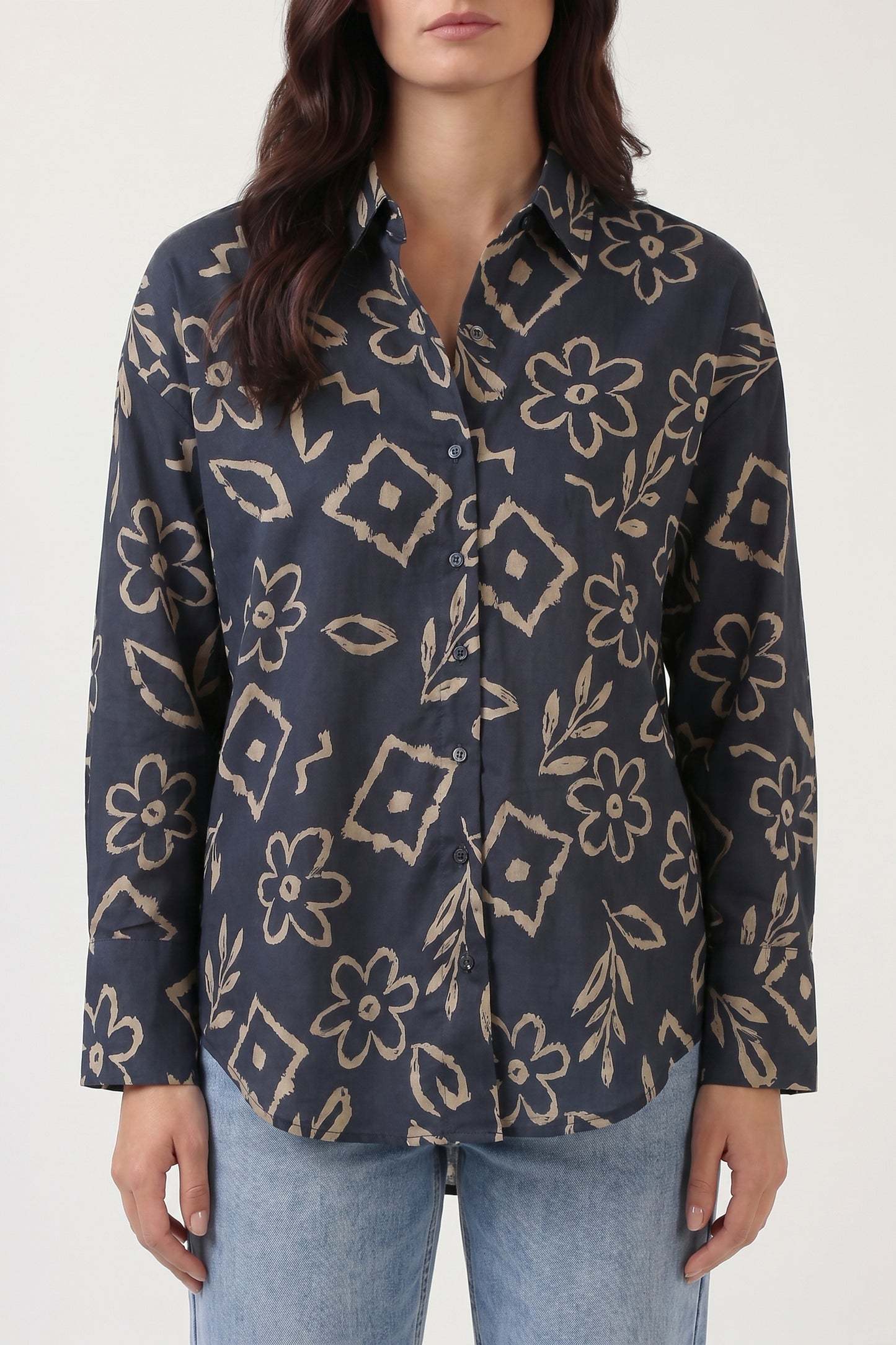 Woman wearing a dark blue patterned shirt with light blue jeans on a white background