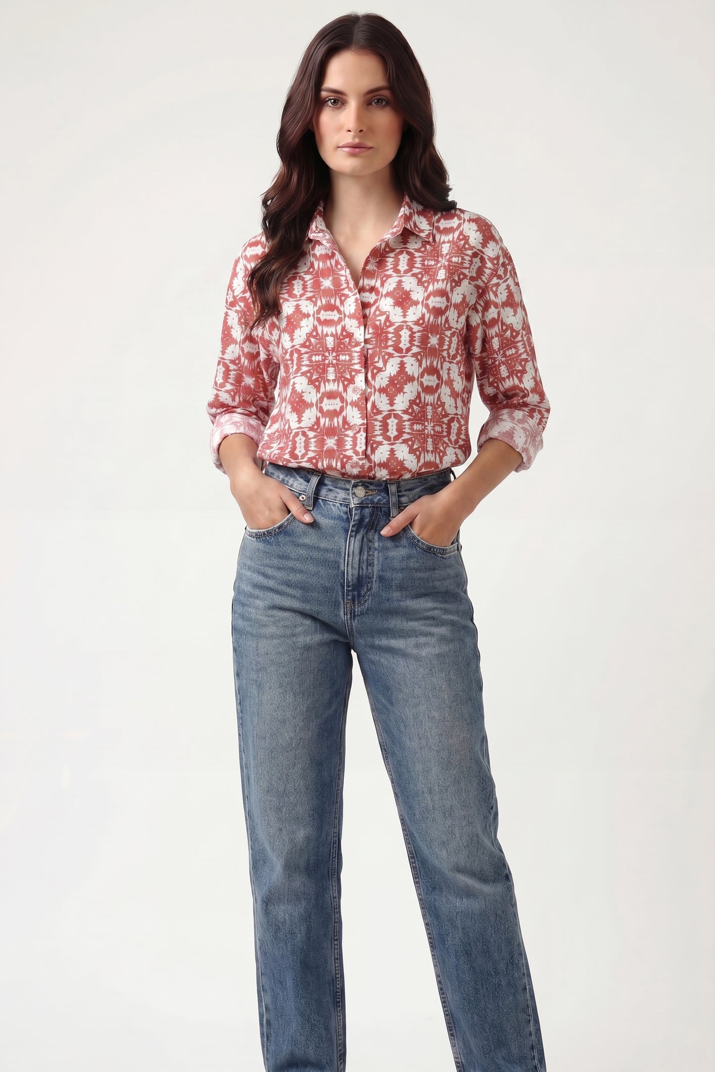 Woman wearing a red patterned blouse and blue jeans on a white background